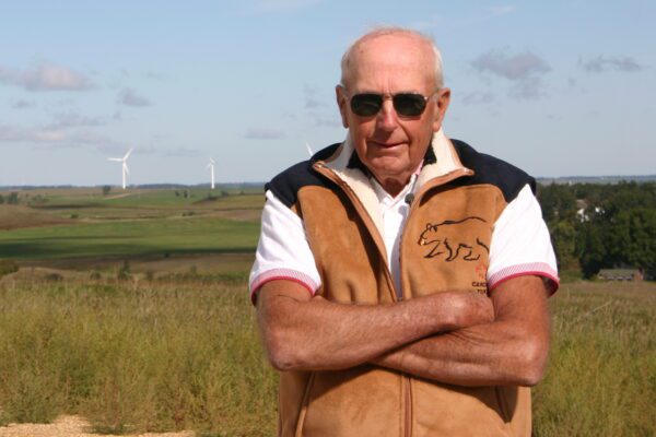Glenn Krog standing at the edge of a grassy expanse with wind turbines in the distance