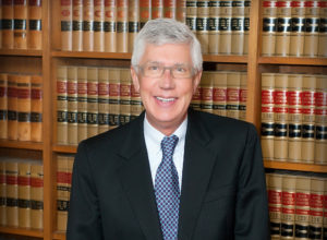 Patrick Costello poses for a formal portrait in front of bookshelves filled with volumes on law.