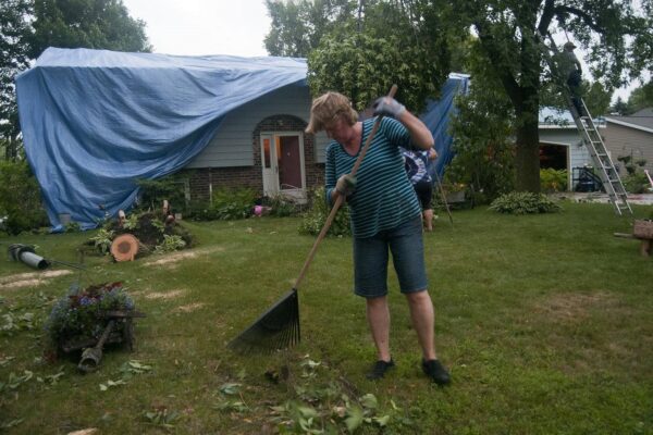 Judy Hulterstrum raking leaves with damaged building in the background
