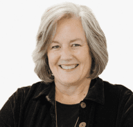 A smiling older woman with gray hair wearing a black jacket and a black top, standing against a plain white background.