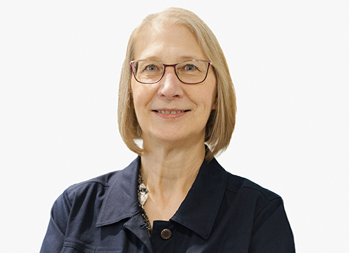 A smiling woman with short blonde hair and glasses, wearing a dark collared shirt, poses in front of a plain, light background.