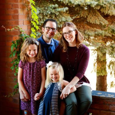 Rob Thurston sits on a ledge outdoors with his wife and their daughters