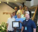 A group of Fey Industries employees hold the plaque honoring the company's Quality Certification Alliance Accreditation.
