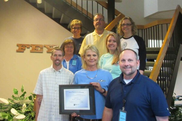 A group of Fey Industries employees hold the plaque honoring the company's Quality Certification Alliance Accreditation.