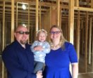Business owners Jason and Mandy Brecher stand in front of the unfinished walls of Oasis Care Home holding their young daughter, Stella