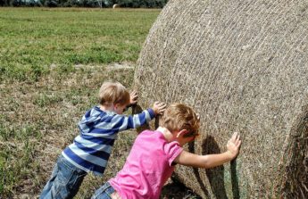 two young children try to roll a large round hay bale in a field