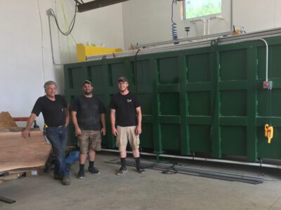 Erwin, Mitch and Justin stand in front of a large green kiln in the shop