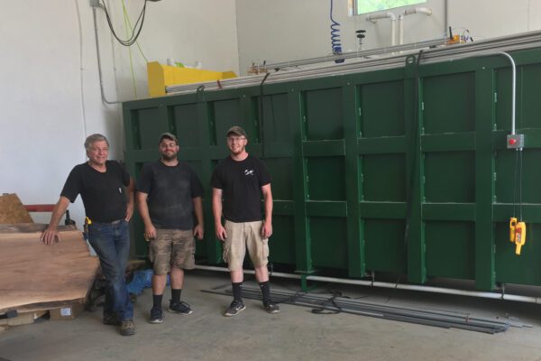 Erwin, Mitch and Justin stand in front of a large green kiln in the shop