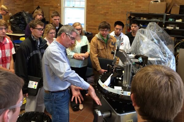 KCEO students gather in a semi-circle around a machine as Nova-Tech Engineering and MinnWest Technology Campus President Jim Sieben explains its function
