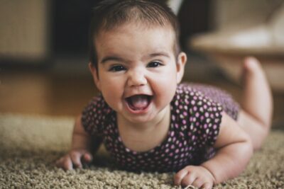 Baby lying on her tummy on a carpeted floor and laughing