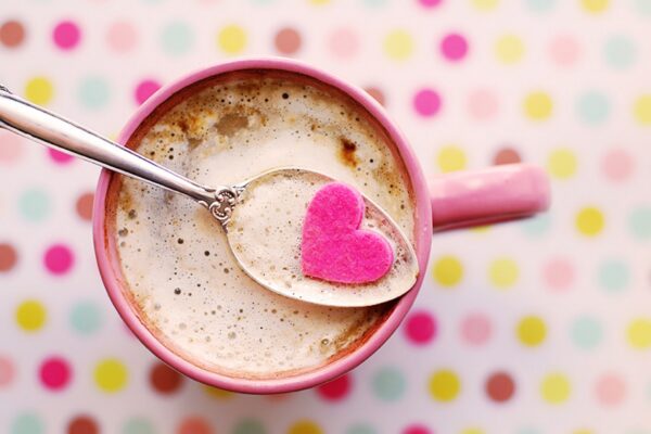 Pink mug of cocoa with a spoon balanced on top and a heart resting on the spoon