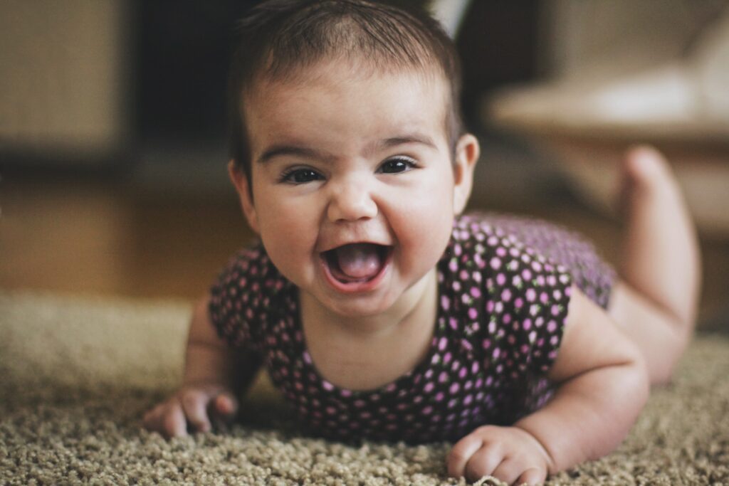smiling baby laying on her tummy on a carpeted floor