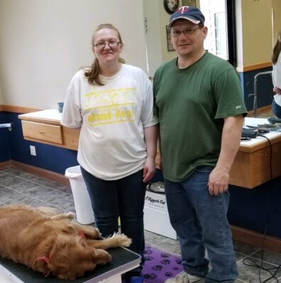 Sarah and Bill stand in the center of their pet grooming business with a dog lying nearby