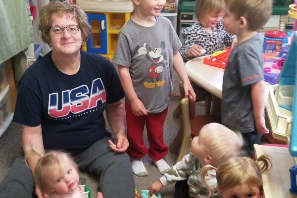 Tammy sits on the floor at her family-based child care surrounded by little kids.