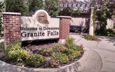 A brick sign surrounded by flowering plants reads "Welcome to Downtown Granite Falls."