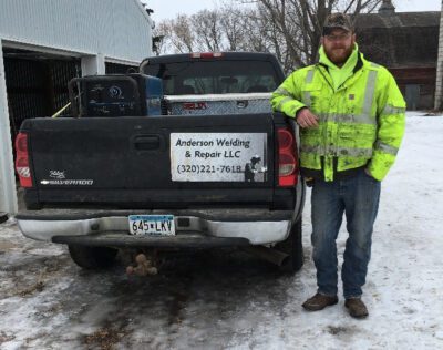 Dillon stands to the right of a black pick-up truck outside in winter.