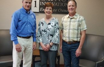 John, Diana and Ron are lined up in an office lobby in front of an Impact Innovation sign