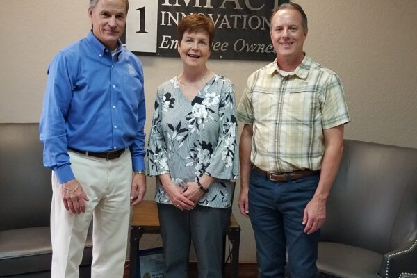 John, Diana and Ron are lined up in an office lobby in front of an Impact Innovation sign