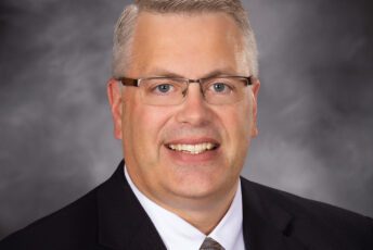 Dan poses for a formal head shot in front of a mottle gray backdrop