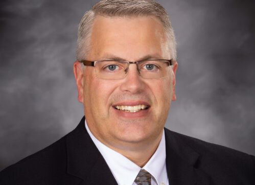Dan poses for a formal head shot in front of a mottle gray backdrop