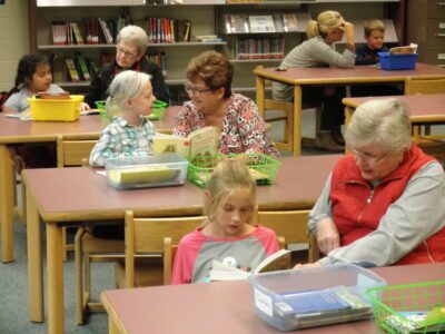Kids and adults read together at tables in a school library