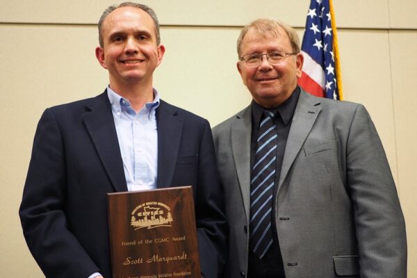 Scott Marquardt and CGMC President Ron Johnson stand shoulder-to-shoulder, with Scott holding a wooden plaque