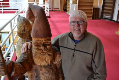 Loren kneels next to a wooden gnome statue in the library
