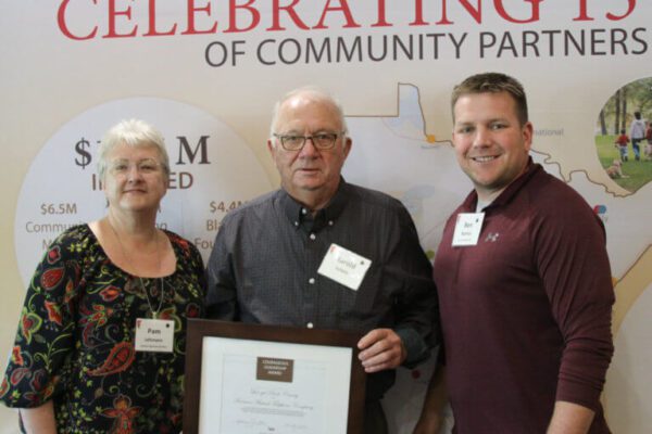 A group of three people pose with a framed award.