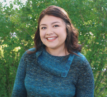 A head shot of Andrea outdoors with foliage in the background
