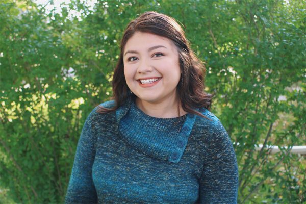 A head shot of Andrea outdoors with foliage in the background