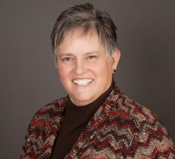 A formal head shot of Theresa in front of a gray background