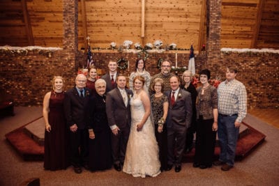 A large family is gathered for a group photo at a wedding