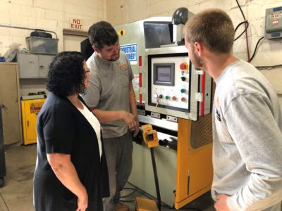 Loan clients Mark and Tobias explain the functions of a piece of manufacturing equipment to Selina