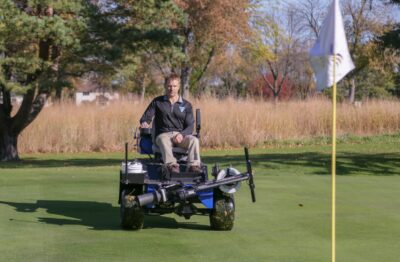 Kevin Froemming drives the Power Assist Cup Cutter across a golf course toward a hole.