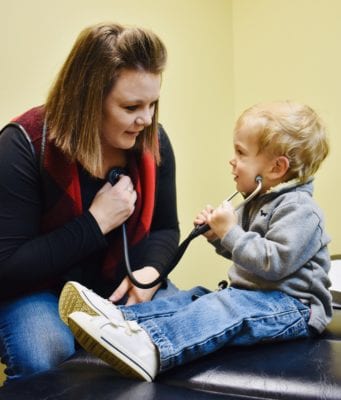Dani holds a stethescope to her chest while her young son listens
