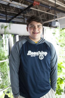 Diego stands in front of vibrant white hydroponic grow towers full of small green plants.