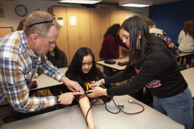 Students practice taking each other's blood pressure with the help of their instructor