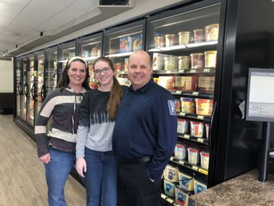 Bill and Kelly stand with their daughter in front of a row of wall freezers