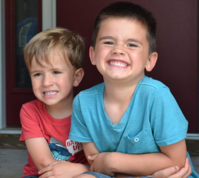 Two young boys sit on a front step close to one another, smiling.