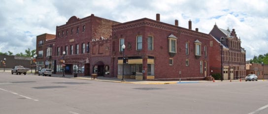Ornate red stone buildings in a downtown district stand against a cloudy blue sky