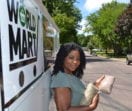 Nathalie leans against her World Mart delivery trailer holding bags of dry goods