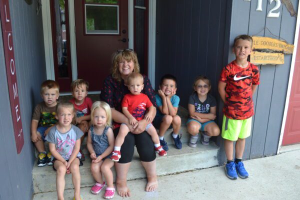 Jane sits outside on her front step with a group of kids, one small boy on her lap