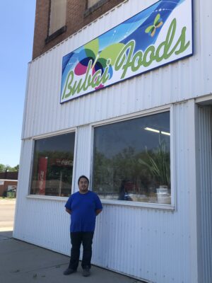 Mark stands outside the front of Bubai Foods grocery store under a colorful sign with the store's name