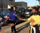 A young black girl in a yellow sweater creates giant bubbles on a sidwalk that another girl is chasing