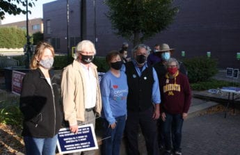 Several adults stand in a line together outdoors wearing masks in downtown Willmar