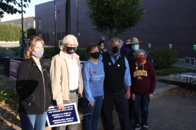 Several adults stand in a line together outdoors wearing masks in downtown Willmar