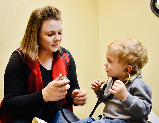 Dani holds the end of a stethoscope while her young son listens