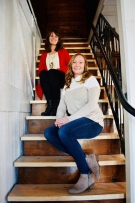 Kayla and Valerie sit on a wooden staircase with iron handrail at Art's Place