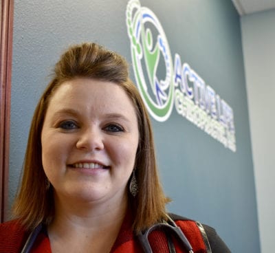 Dani stands in the lobby of her office in front of a wall with her logo displayed