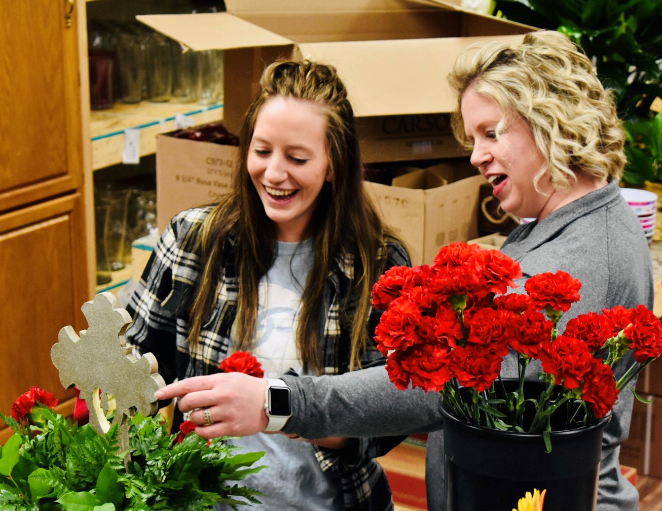 Gina and Kendra arrange red carnations and greenery around a cross